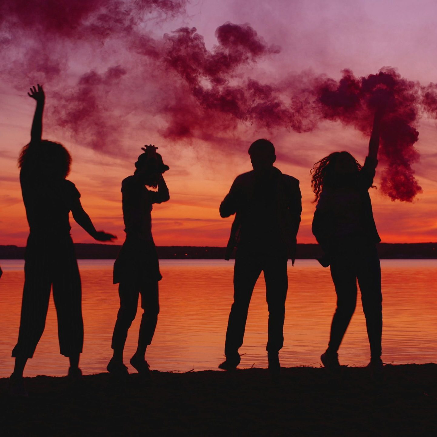 silhouetted young people on a beach holding smoke bombs