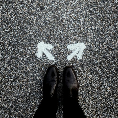 Feet standing on tarmac in front of two arrows facing different ways.